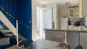 A modern kitchen with a refrigerator, microwave, and toaster. There is a dining area with a table and chairs. A staircase with blue walls leads to another room. - Family home near beach with WiFi and pets allowed (La Tranche-sur-Mer)