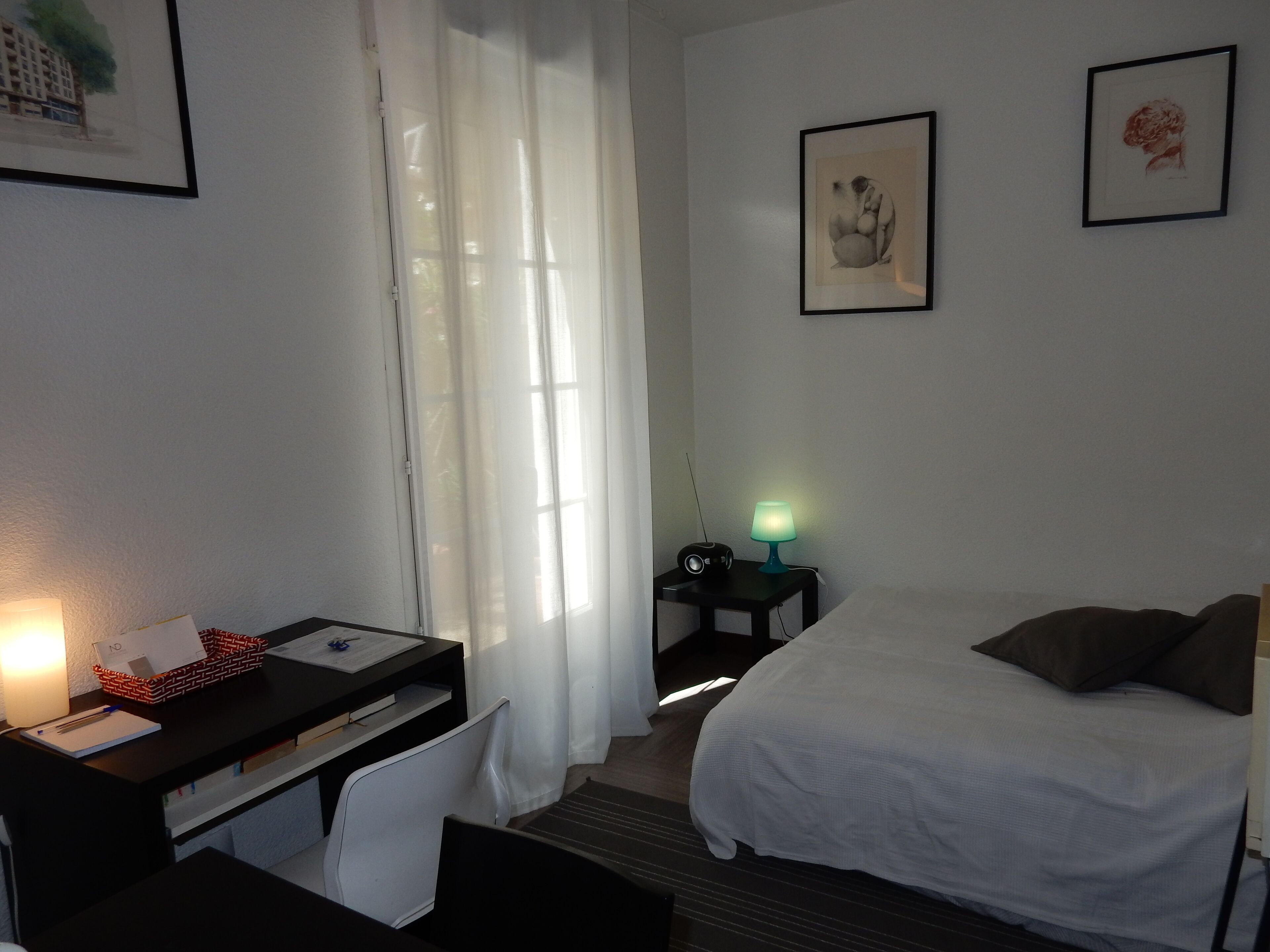 Een hotelkamer met een bed, een bureau met stoel, een lamp en twee ingelijste foto's aan de muur.