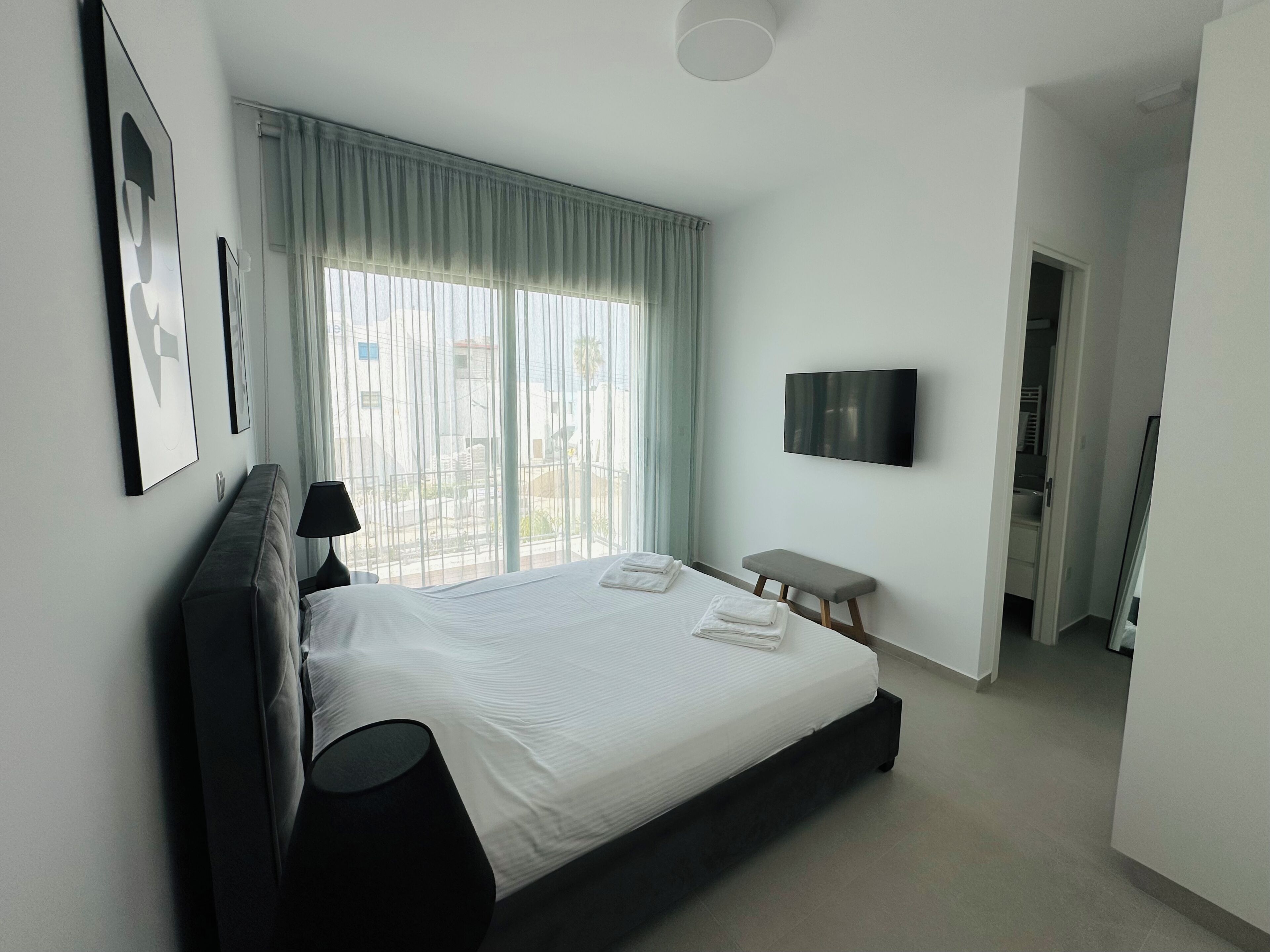 Et moderne hotelværelse med en stor seng, et fladskærms-tv, en bænk og udsigt ud.