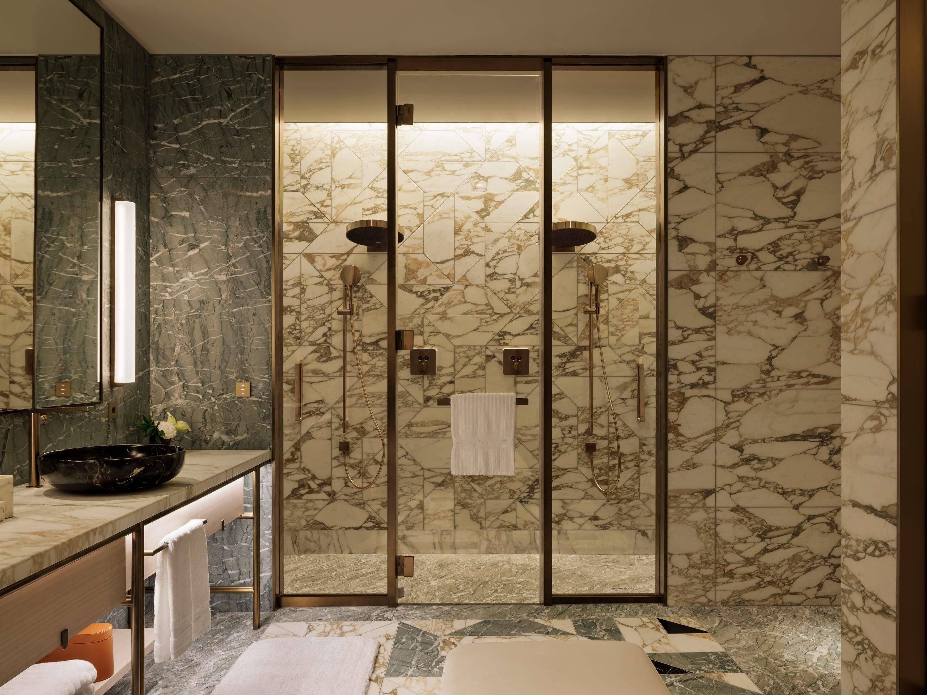 A modern bathroom with a glass-enclosed shower, marble walls, and a vanity with a sink and mirror.