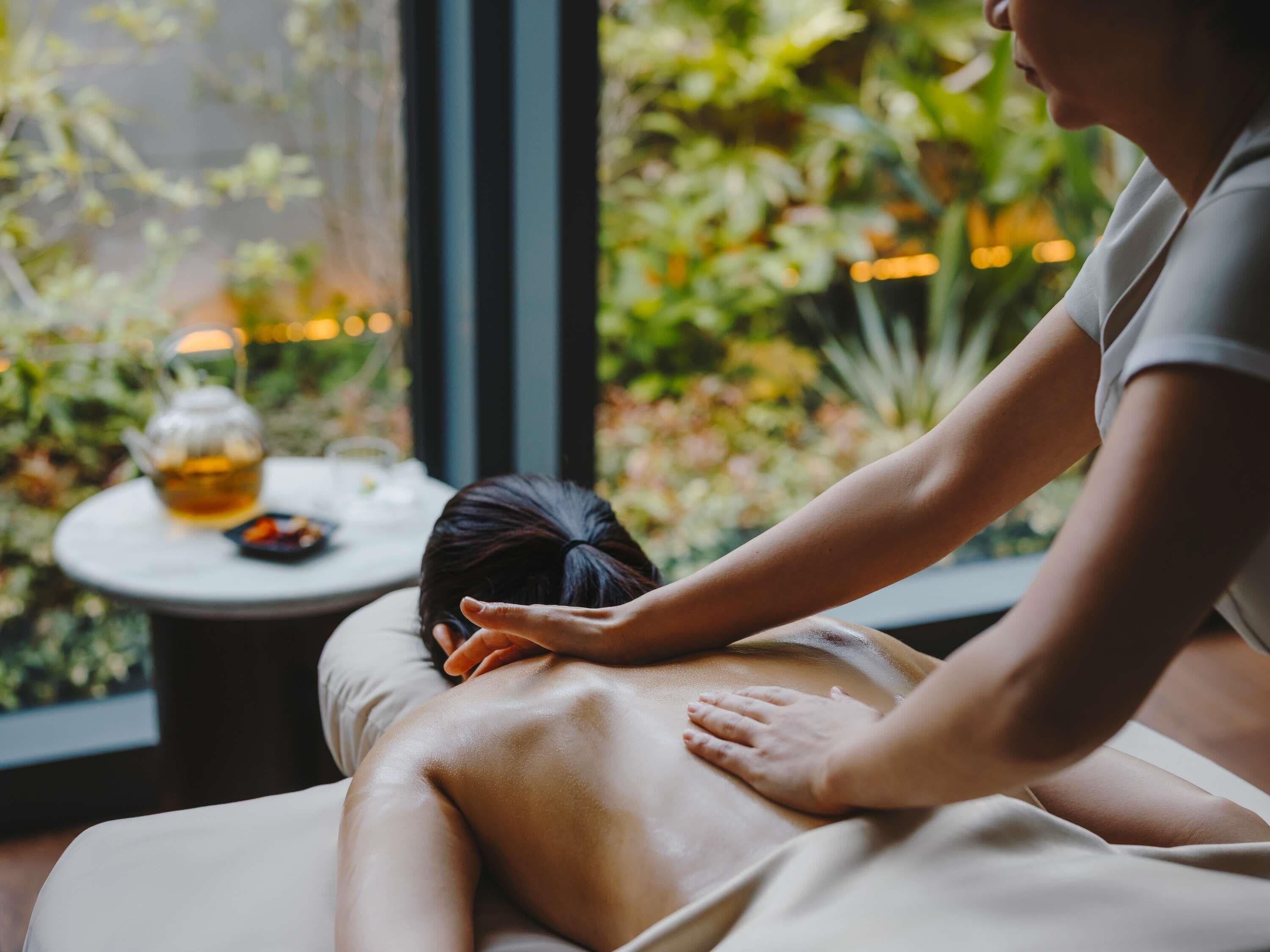 Sesión de masoterapia en una habitación con vistas a zonas verdes y una mesa con un calentador de agua.