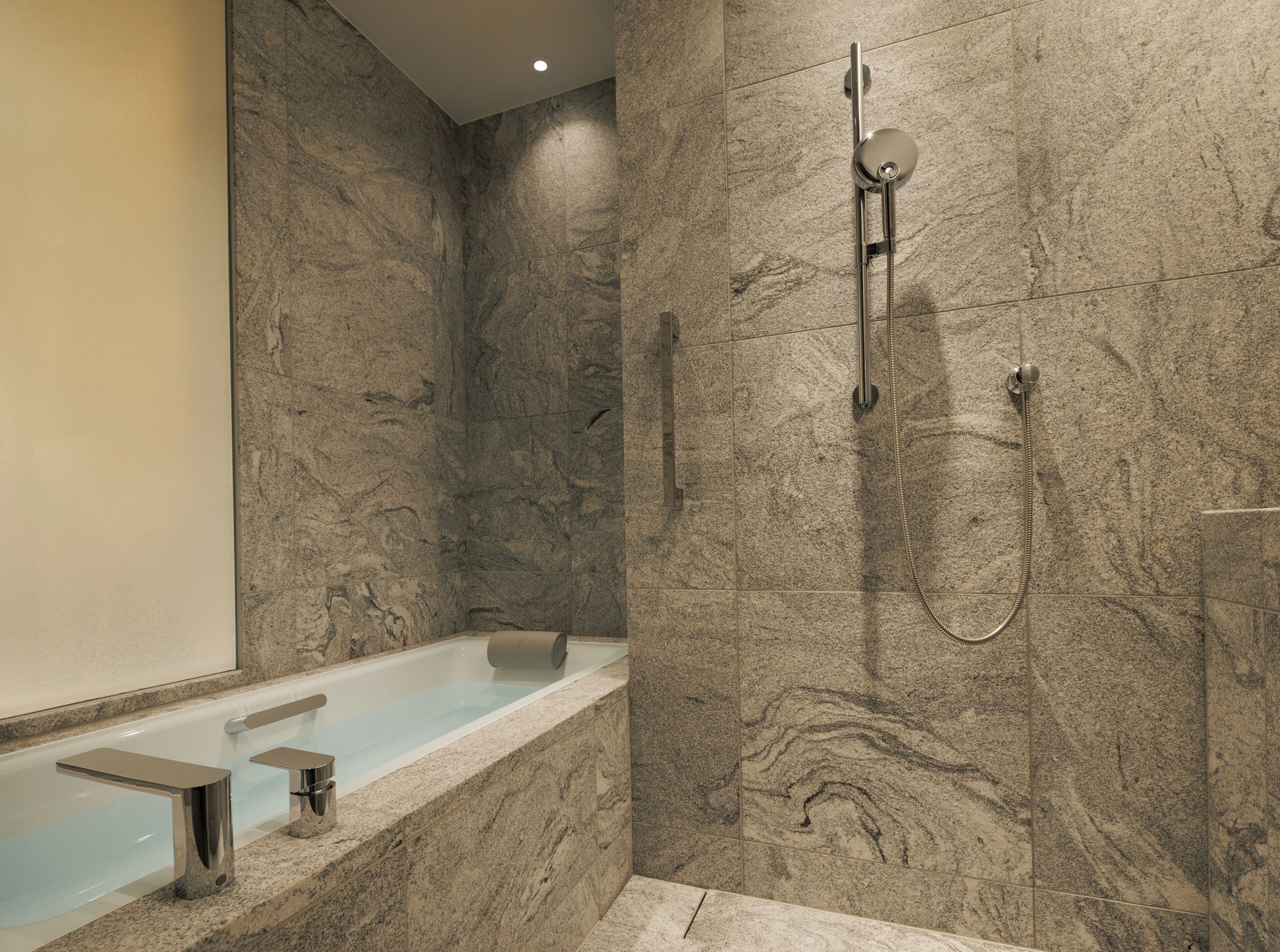 A modern bathroom with a marble wall, a freestanding bathtub, and a shower with a handheld showerhead.