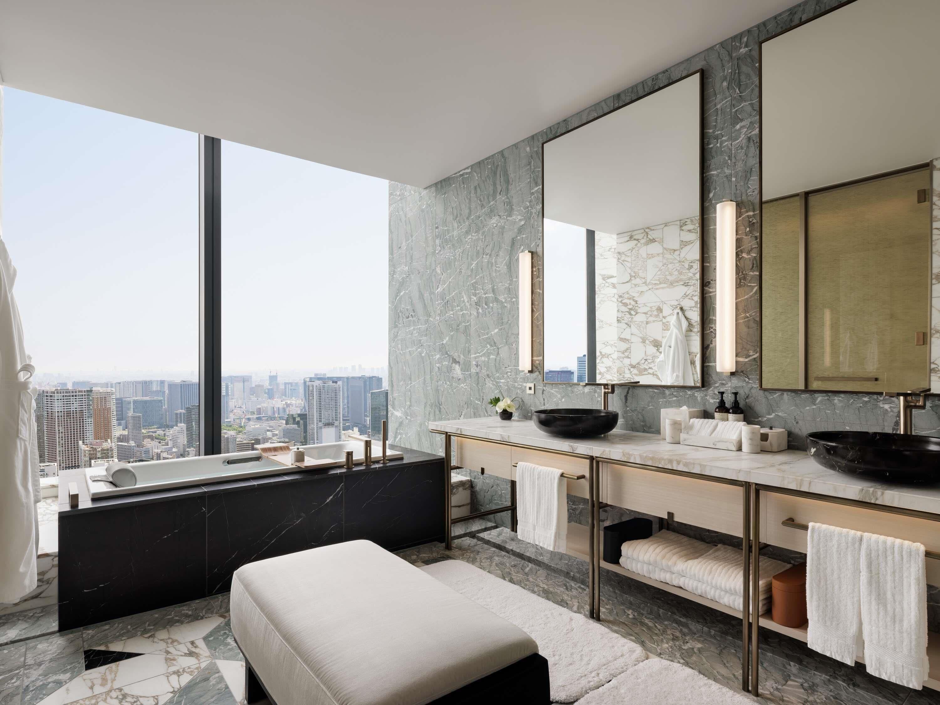 A modern bathroom with a large window, a bathtub, two sinks, and a large mirror.