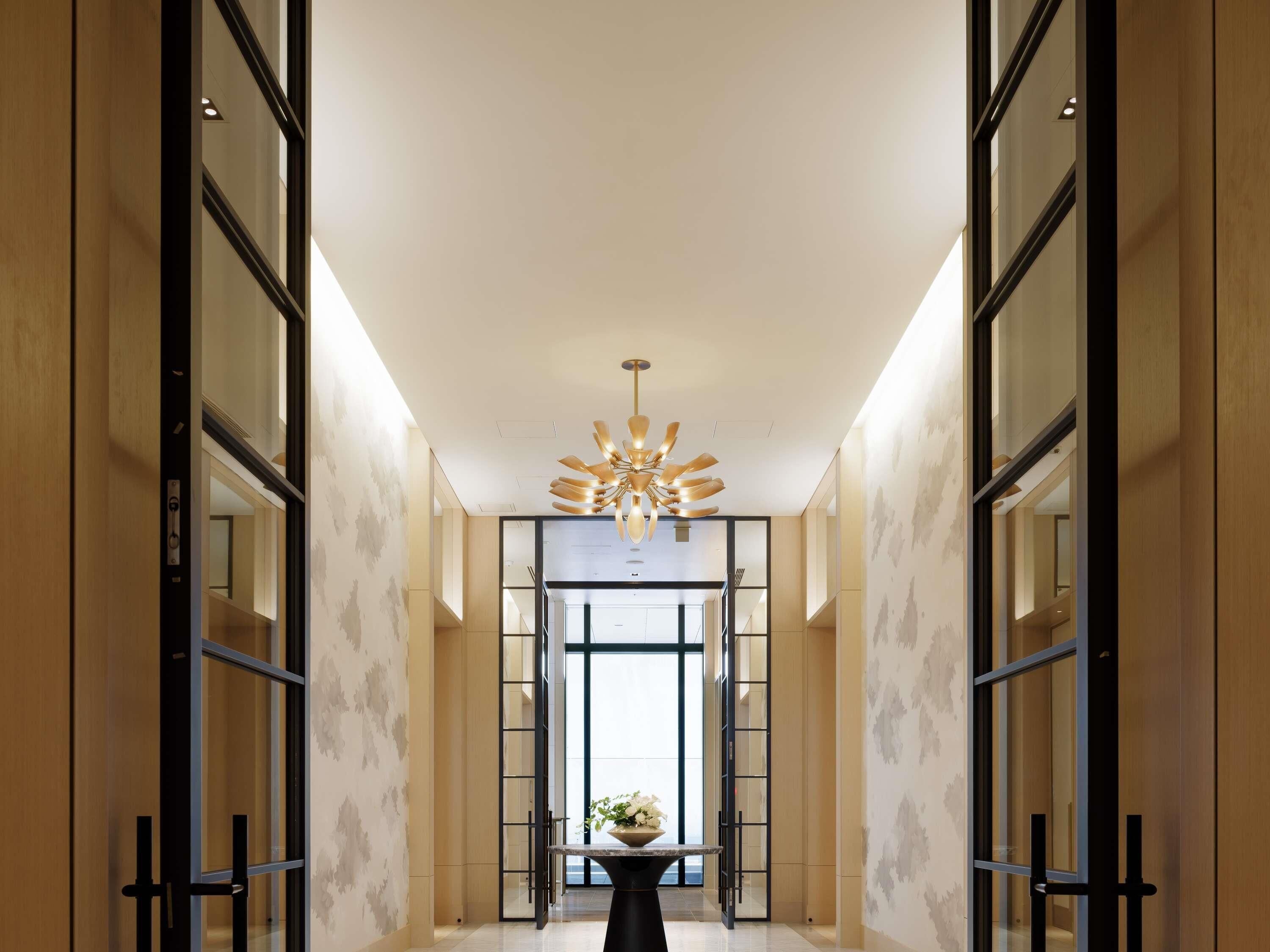 A modern hotel lobby with a central chandelier, mirrored walls, and a marble floor.