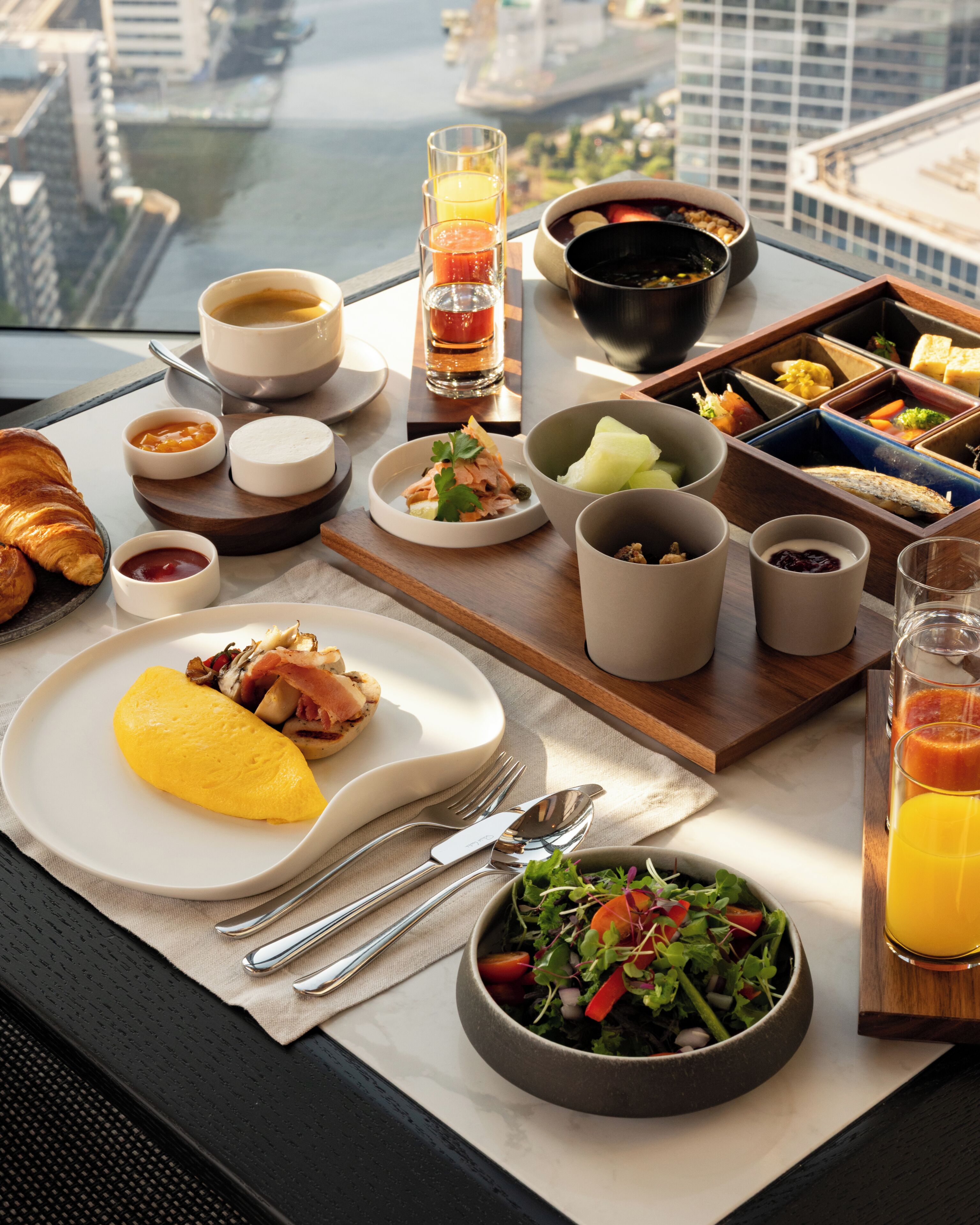 A breakfast buffet with various dishes, a croissant, and a city view.
