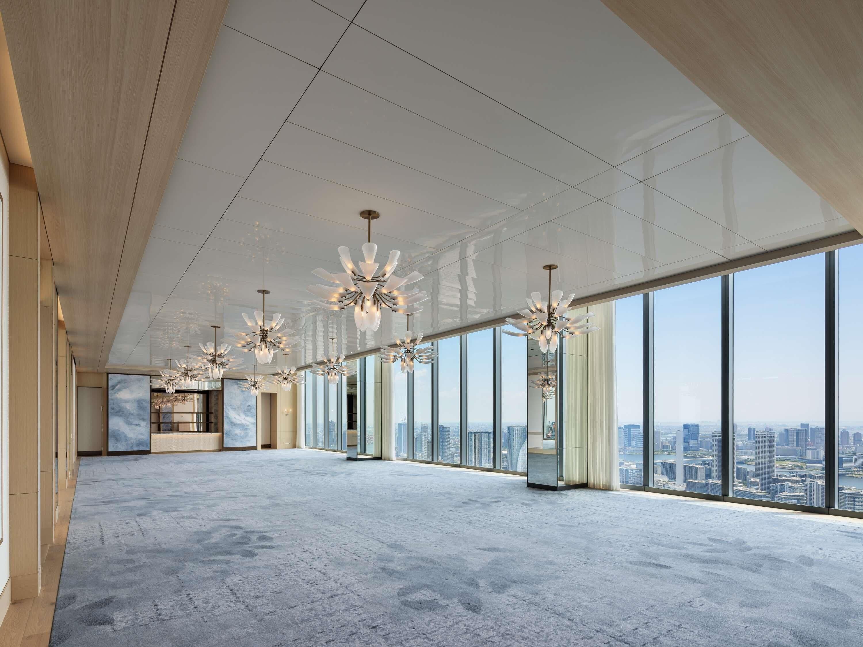 A spacious, high-ceilinged interior with large windows offering city views, modern chandeliers, and a minimalist design.