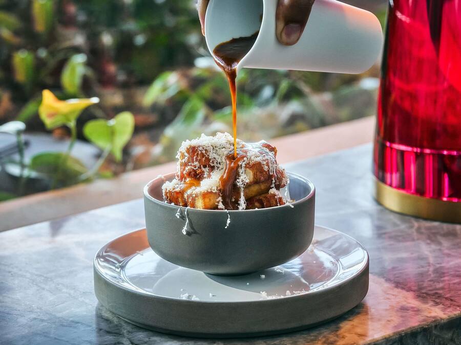 A bowl of food with sauce being poured over it, placed on a plate on a table.