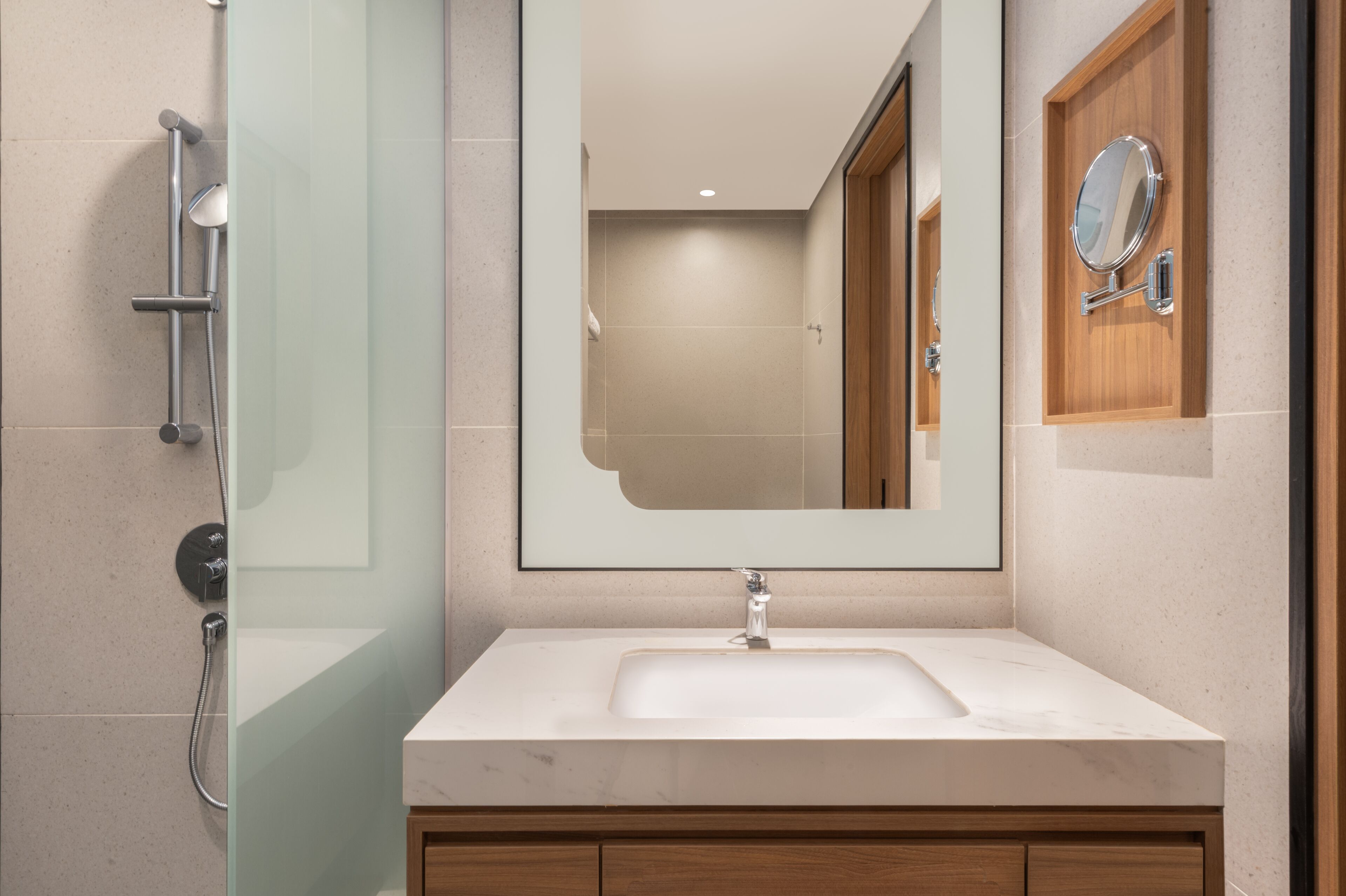 A modern bathroom with a glass shower enclosure, a large mirror, and a wooden vanity with a sink.