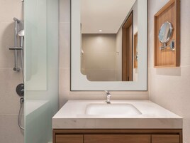 Un baño moderno con cabina de ducha de vidrio, un espejo grande y un tocador de madera.