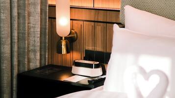A neatly made bed with white linens and a heart-shaped pillow, a bedside table with a lamp, and a wooden panel wall.