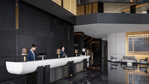 A modern reception area with a long reception desk, two receptionists, and a seating area with a sofa and coffee table. - Grand Mercure Batam Centre (Batam)
