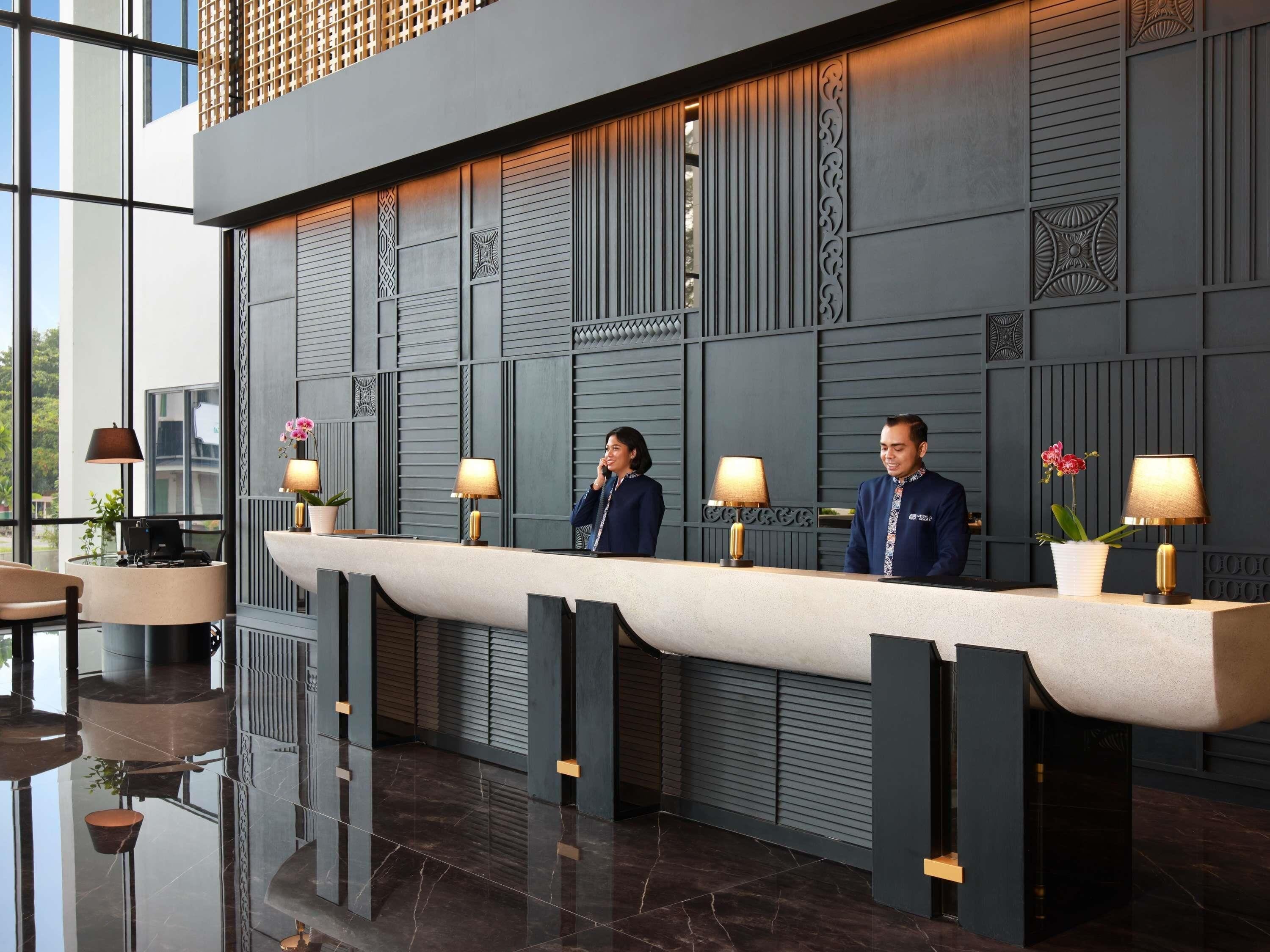A reception desk with a modern design, featuring a long counter, two receptionists, and decorative lamps.