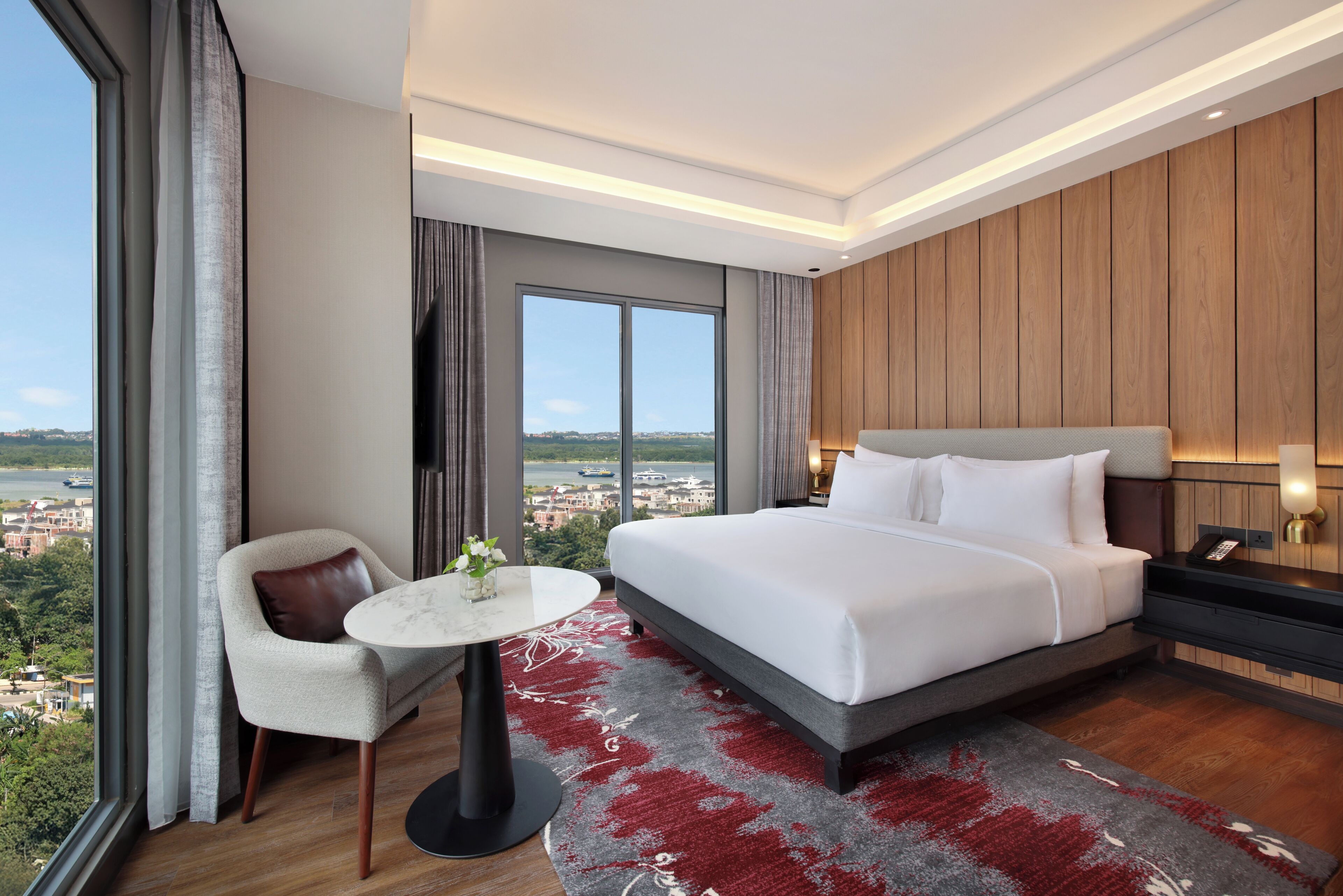 A hotel room with a large bed, a chair, a small table, and a view of the city.