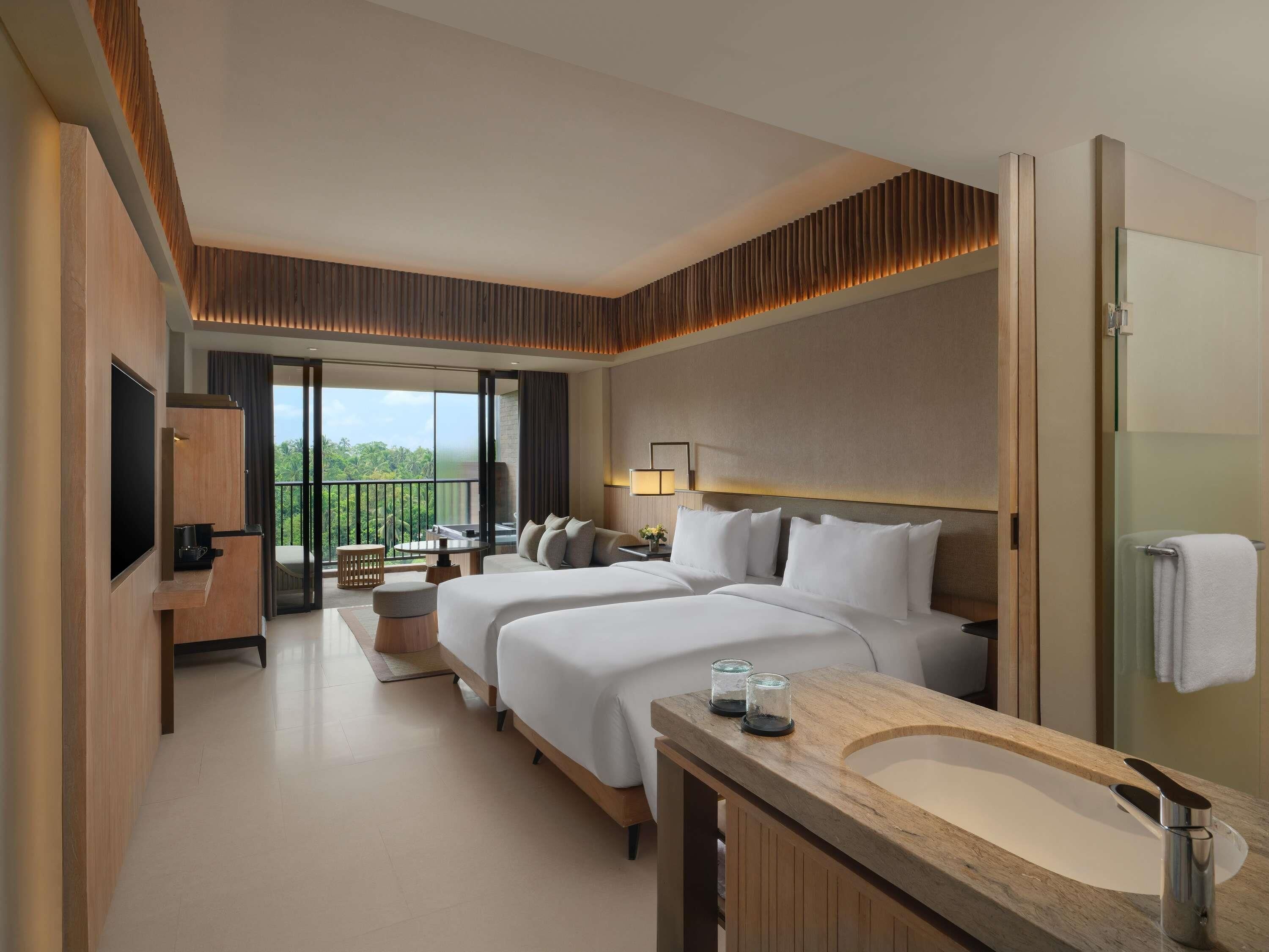 A hotel room with a large bed, a sitting area with a table and chairs, a TV, and a bathroom with a sink and mirror.