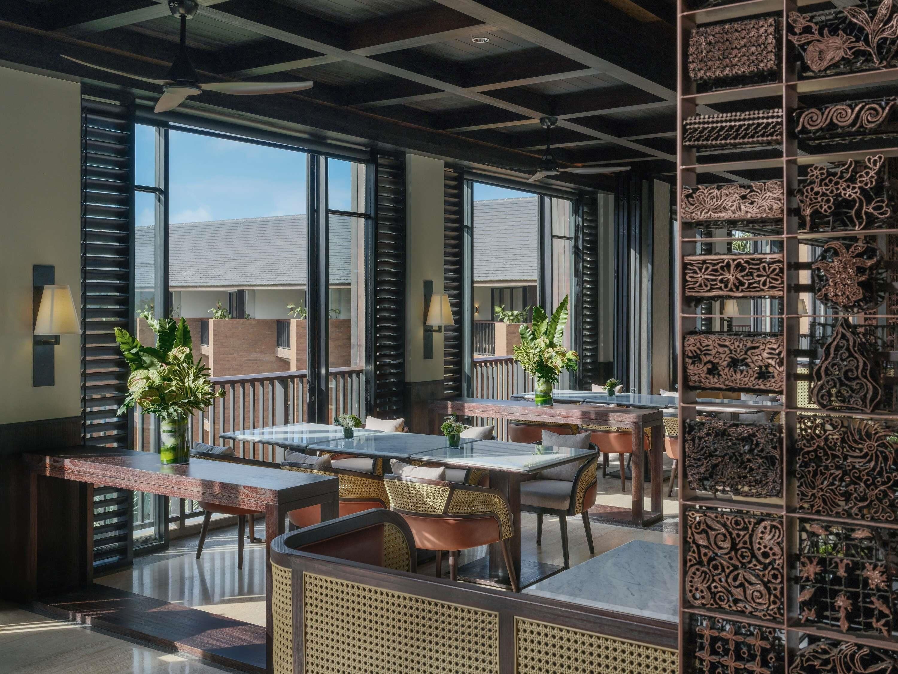 Un vaste espace extérieur aménagé pour les repas, avec de nombreuses tables et chaises, de grandes fenêtres et des panneaux muraux décoratifs.