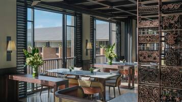 A spacious outdoor dining area with multiple tables and chairs, large windows, and decorative wall panels.