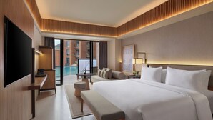 A modern hotel room with a large bed, a flat-screen TV, a desk, and a view of a swimming pool and building. - Novotel Bali Ubud Resort (Payangan)