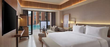 Habitación de hotel moderna con una cama grande, televisión de pantalla plana, escritorio y vistas a una piscina y un edificio.