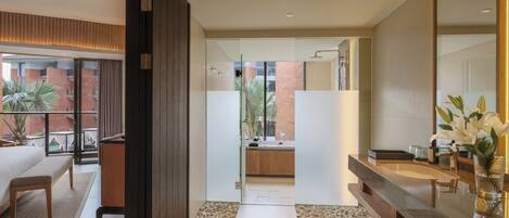 A modern hotel room with a balcony, a large mirror, and a bathroom with a shower and sink.