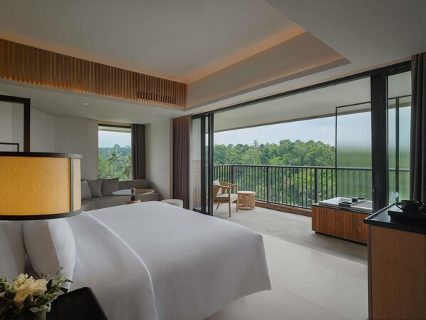 A hotel room with a large bed, a desk, a chair, and a balcony with a view of the forest. - Novotel Bali Ubud Resort (Payangan)