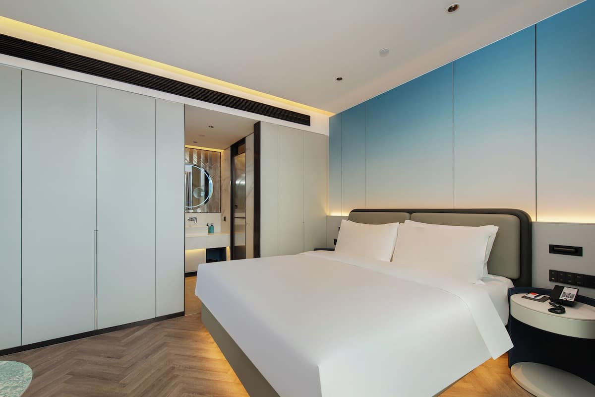 A modern hotel room with a large bed, a bedside table with a phone, and a wardrobe.
