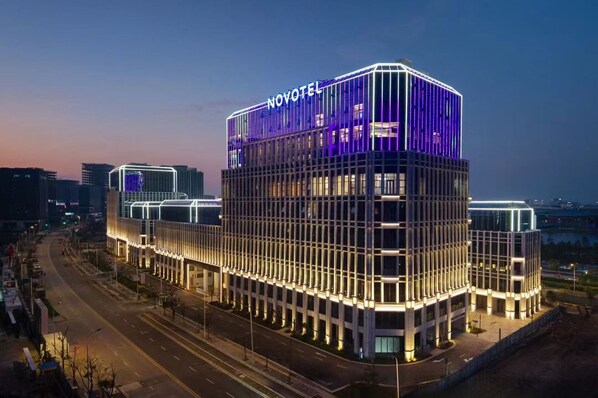 Um hotel moderno com um letreiro grande de 'NOVOTEL', apresentando uma fachada em estilo de grade e janelas iluminadas.