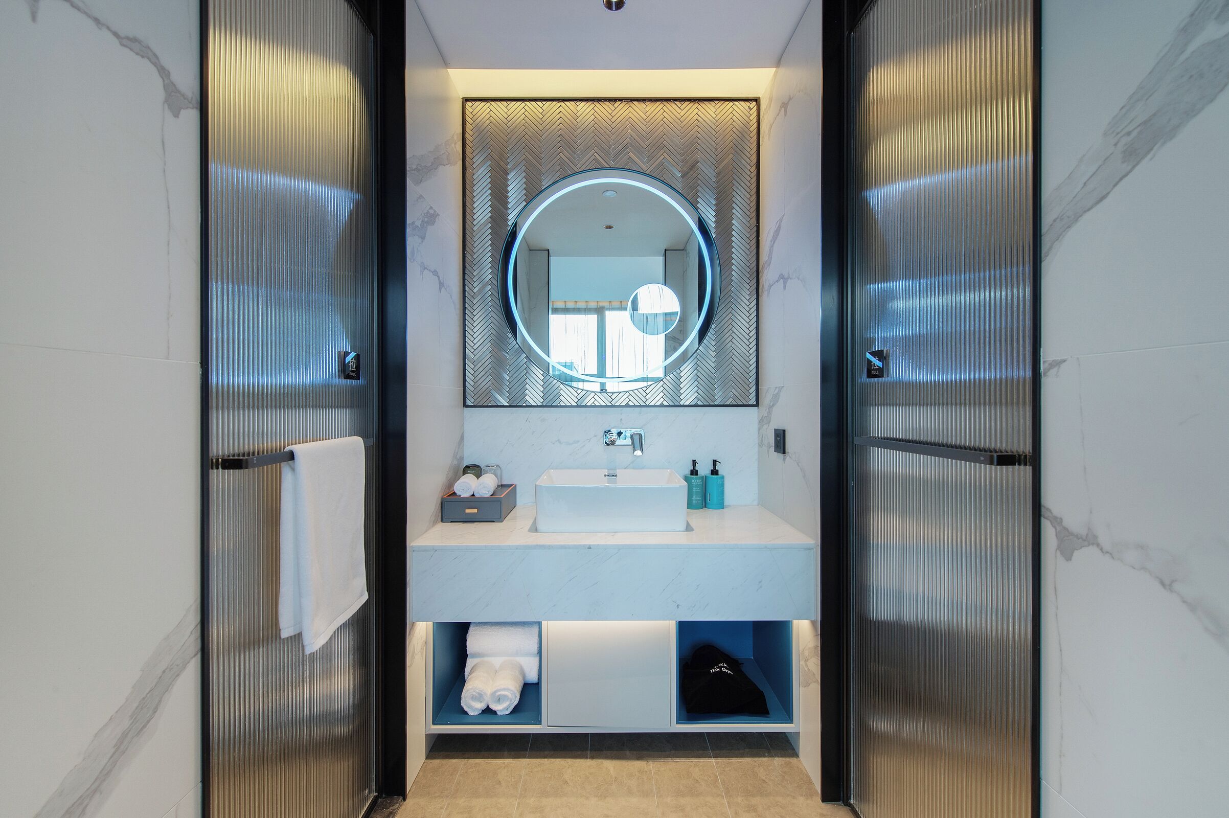 A modern bathroom with a round mirror, white sink, and built-in shelves.
