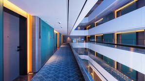 Un pasillo moderno de hotel con barandillas de cristal, piso estampado e iluminado.