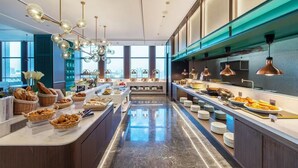 Un desayuno buffet moderno con gran variedad de alimentos, una isla central y vistas a la ciudad a través de amplias ventanas.