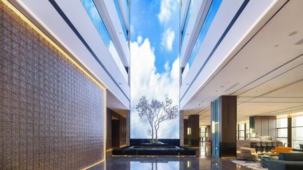 Un vestíbulo moderno con un techo que simula el cielo digital, una recepción y una zona de estar.