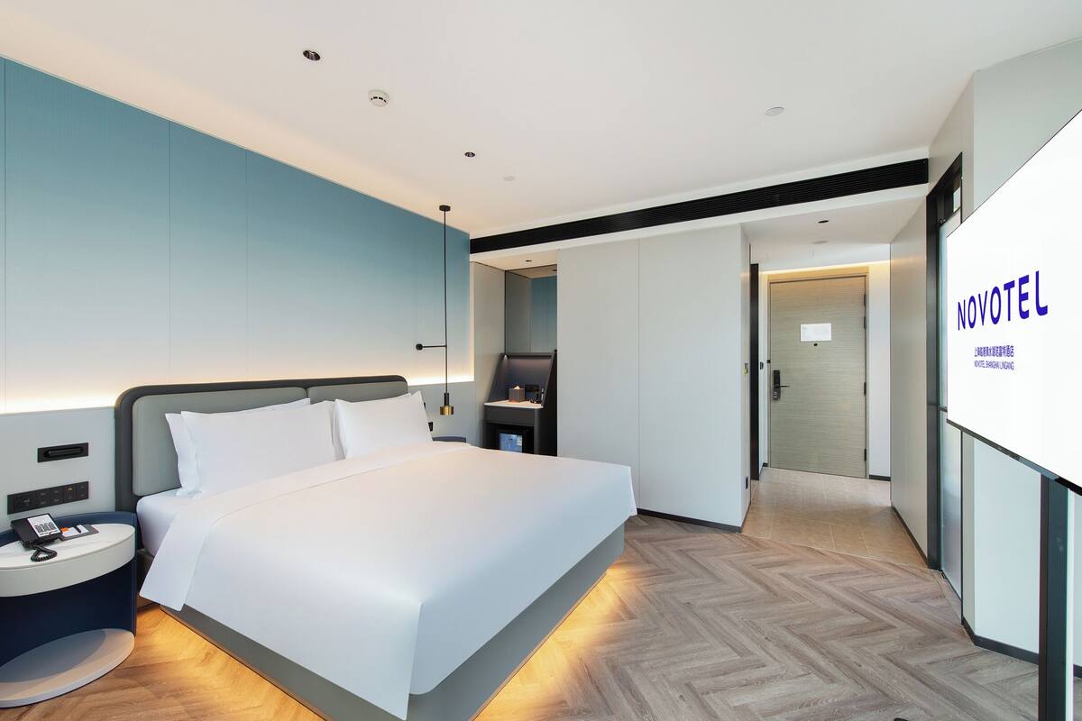 A modern hotel room with a large bed, bedside tables, a desk, and a wardrobe.