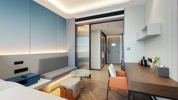 Una habitación de hotel moderna con sofá, una pequeña mesa redonda, una mesita de centro, un área de comedor con mesa y sillas, y una kitchenette.