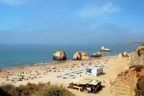 Ein Strand mit großen Felsformationen, vielen Sonnenschirmen und einem kleinen Imbisswagen.