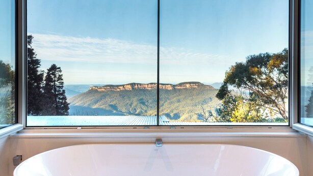 Un baño con una bañera grande y vistas a un paisaje montañoso a través de una ventana.