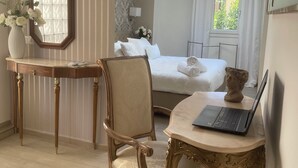 Habitación de hotel con cama, escritorio con computadora portátil, silla, jarra con flores y ventana con cortinas.
