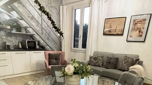 Una sala de estar moderna con una mesa de comedor de vidrio rodeada por sillas tapizadas en gris, un sofá gris y una lámpara de araña.