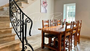 A dining area with a wooden table and chairs, a staircase with a black railing, and a window with natural light. - Le Gîte des Sabotiers by Kastell Breizh (Canihuel)