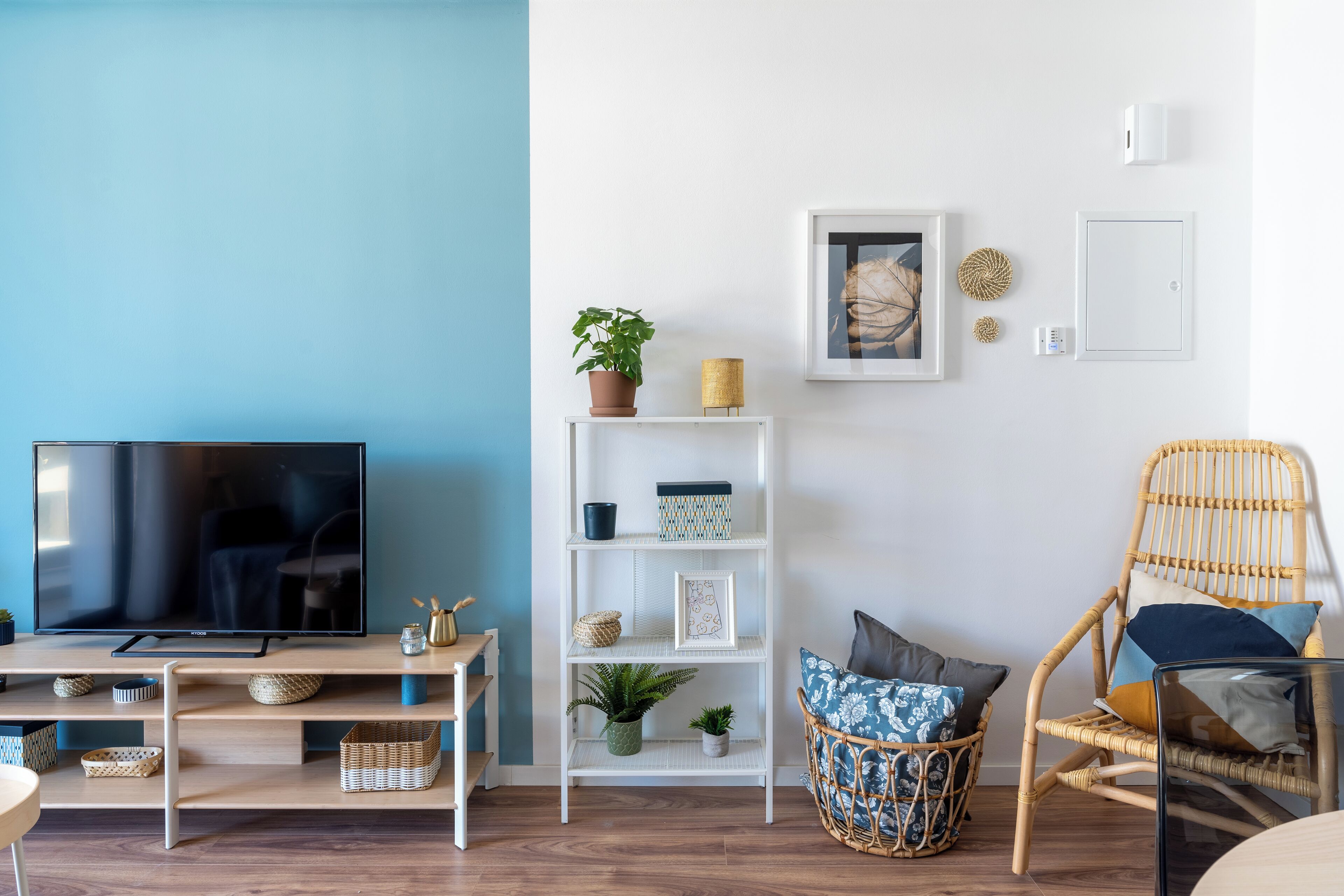 A living room with a TV, white shelves, wicker furniture, and a blue wall.