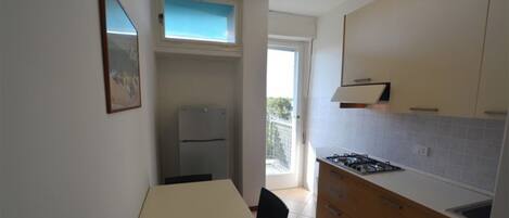 A compact kitchen with a dining table, a refrigerator, a gas stove, and a small balcony.
