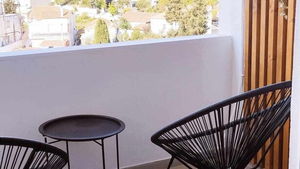 A balcony with two black wire chairs and a small round table. A potted plant hangs on the wall.