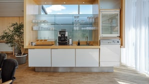 Cozinha moderna com prateleiras de vidro, cafeteira e máquina de lavar loiça.