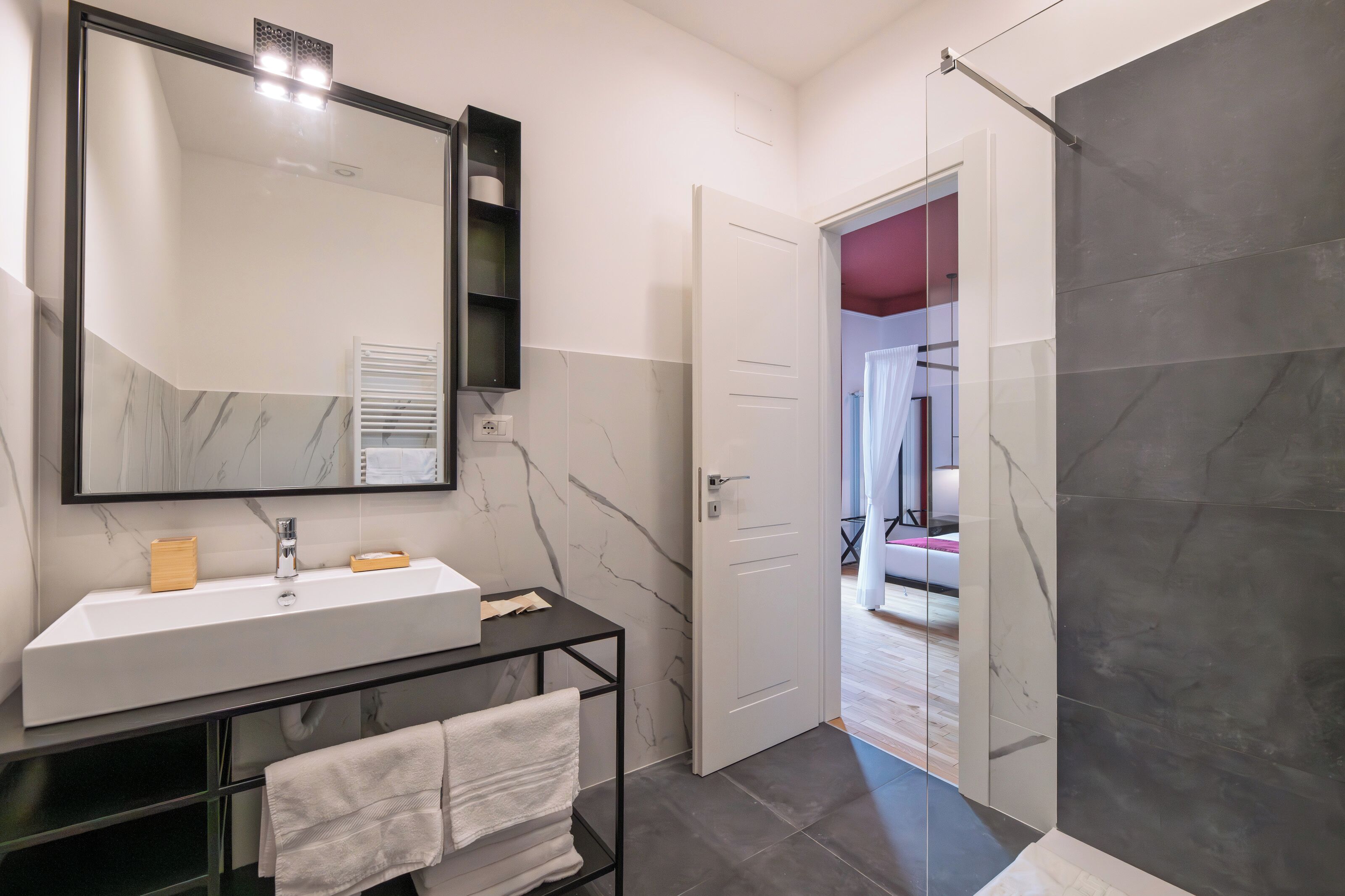 Een moderne badkamer met een grote spiegel, een witte wastafel en een zwart aanrecht.