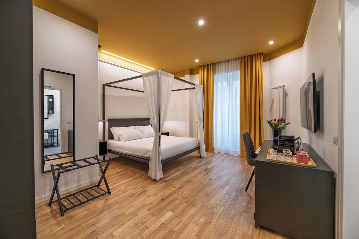 A modern bedroom with a four-poster bed, a desk with a tray, and a large mirror.