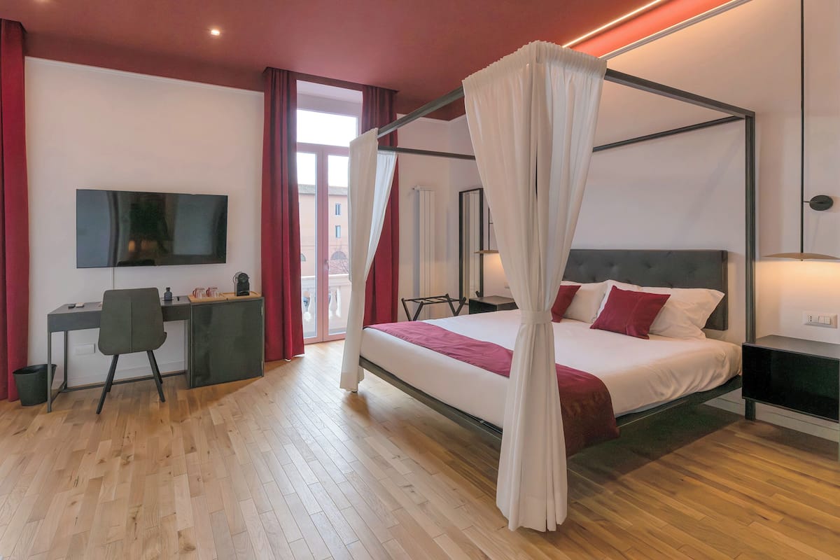 A modern bedroom with a four-poster bed, a desk, and a television.