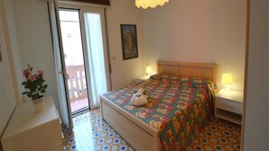 A bedroom with a bed, bedside lamps, a potted plant, and a door leading to an outdoor area. - Central Apartment Near the Beach With Parking (Lignano Sabbiadoro)