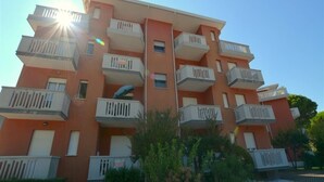A multi-story residential building with balconies, a central stairwell, and a clear sky. - Central Apartment Near the Beach With Parking (Lignano Sabbiadoro)