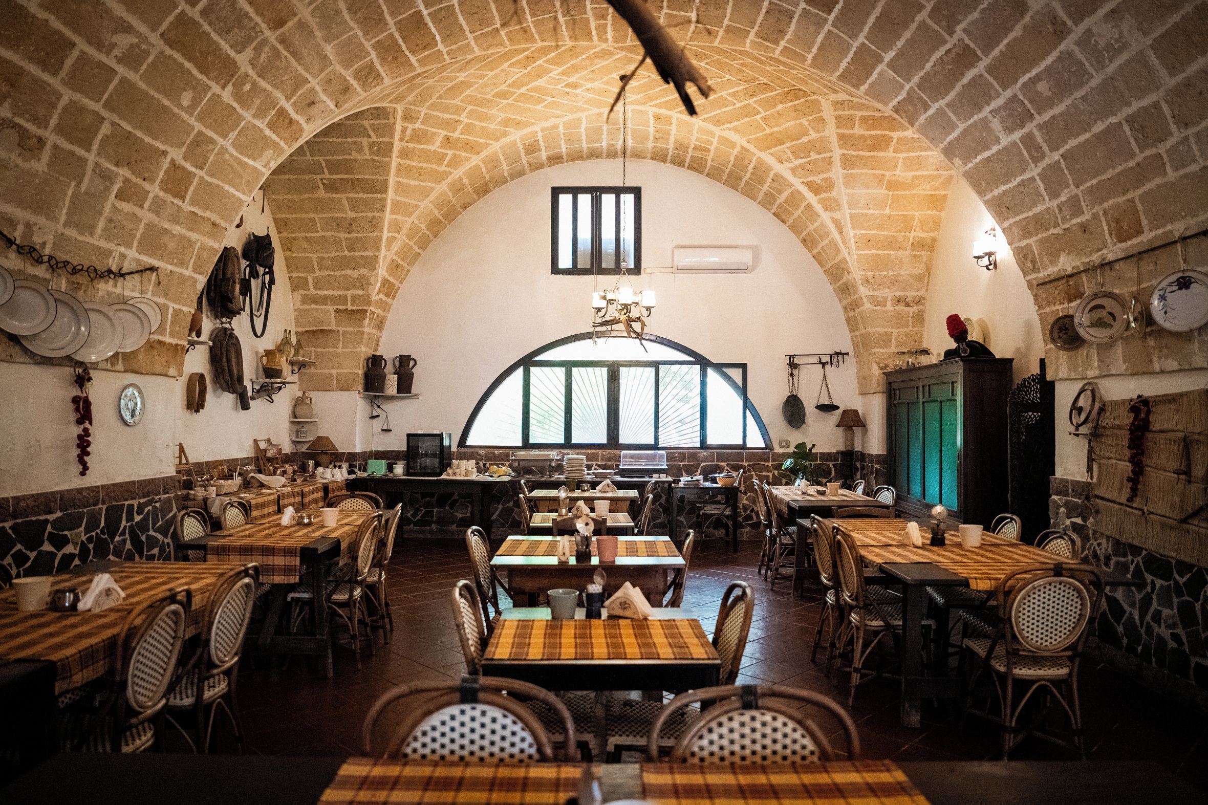 A restaurant with a high arched brick ceiling, multiple tables and chairs, and a large window with a view.