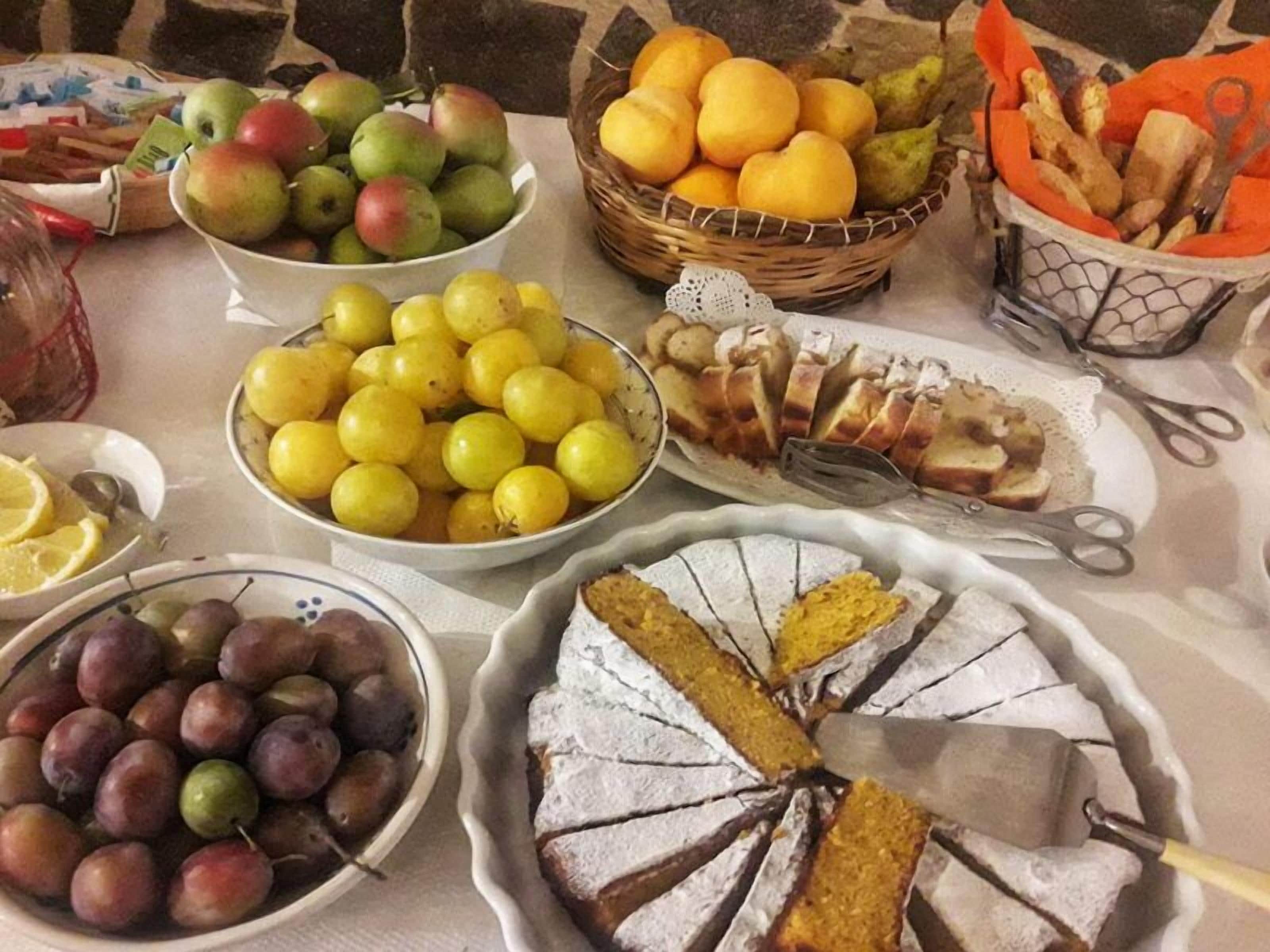 Una mesa con diversas frutas, como manzanas, limones y uvas, y un pastel con un cuchillo encima.