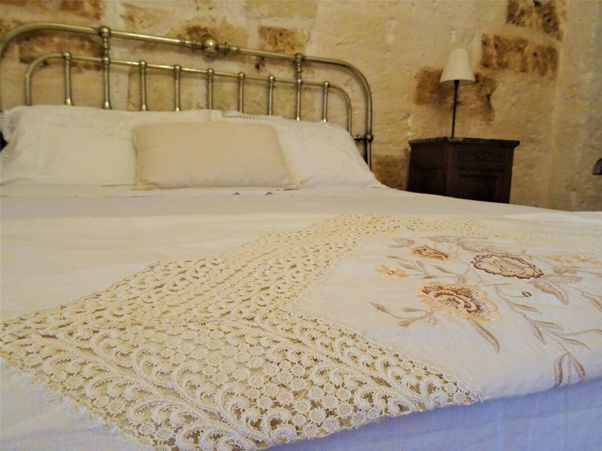 A bed with a floral bedspread and a lace border, a metal headboard, and a nightstand with a lamp.