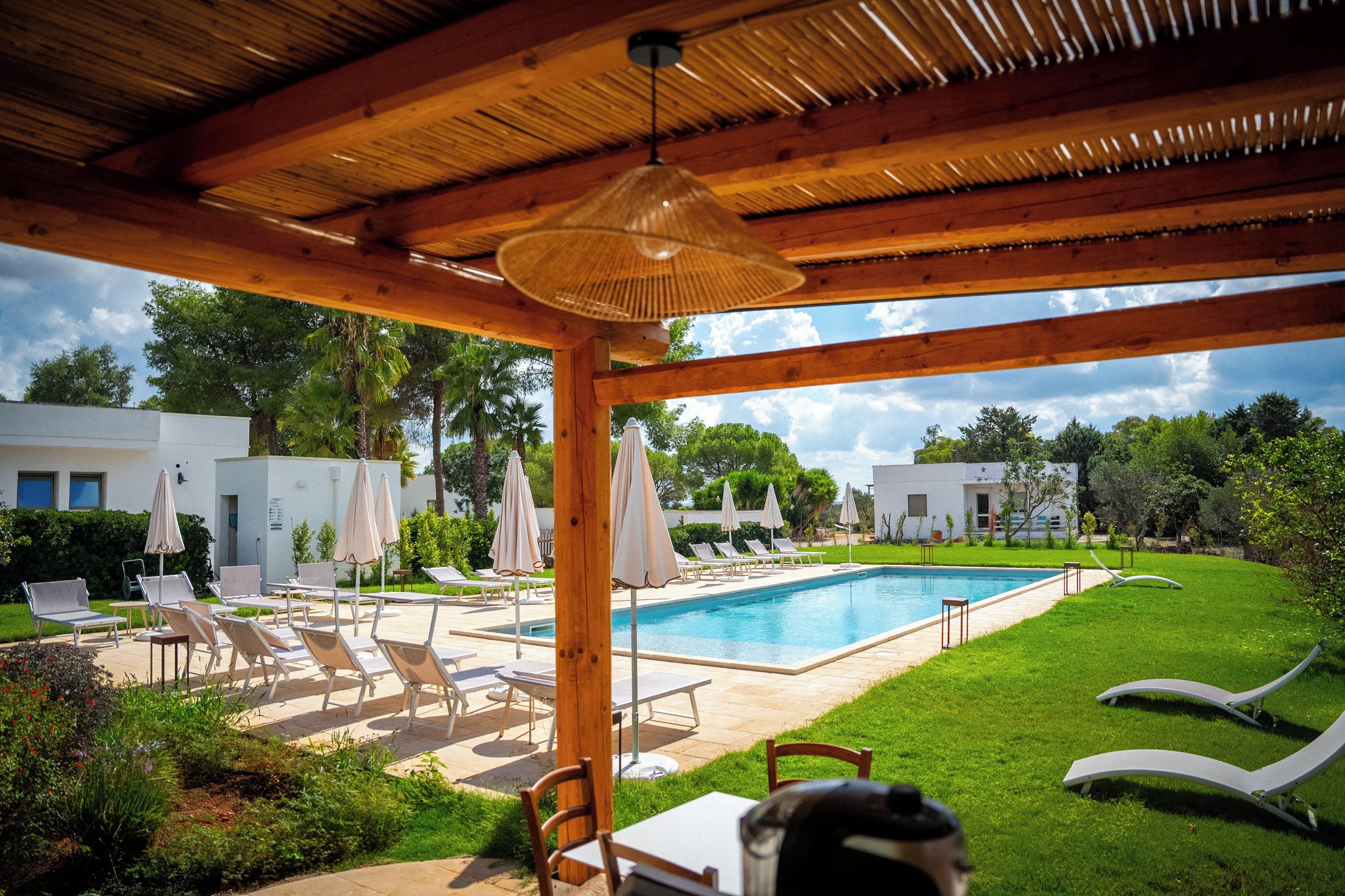 A pool area with lounge chairs and umbrellas, a covered seating area, and a view of the surrounding landscape.